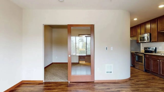 Interior view of an apartment with a sliding glass door leading to another room and a view of the kitchen.