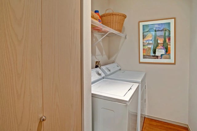 Stackable washer and dryer in a laundry closet with shelving and artwork.
