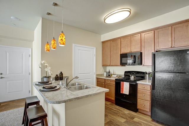 Kitchen with granite countertops, stainless steel sink, pendant lights, and black appliances.