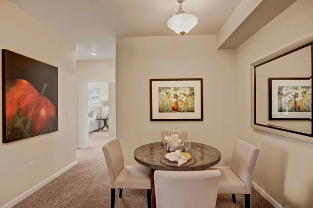 Dining area with a round table and four chairs, artwork on walls, view into bedroom.