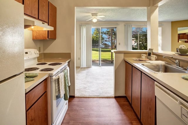 Kitchen with white appliances, wooden cabinets, and a view of the living area and backyard.