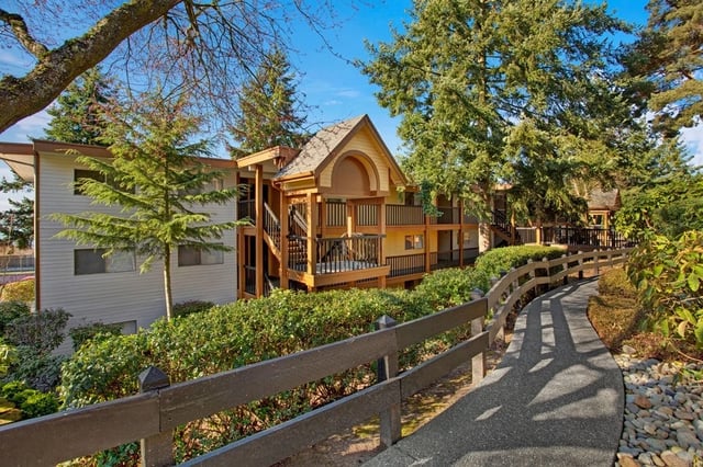 Apartment building exterior with a paved walkway and wooden fence.