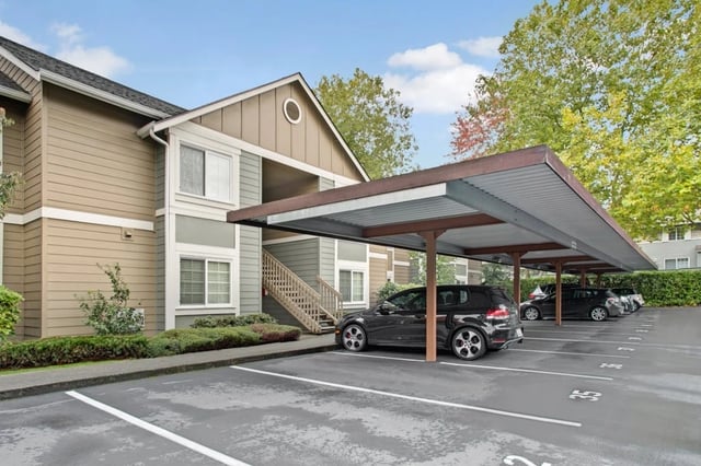 Covered parking spaces with cars parked, adjacent to apartment building.