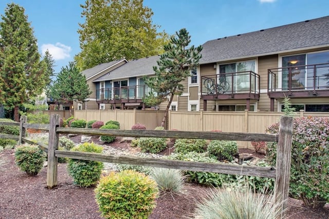 Exterior view of apartment buildings with balconies and a wooden fence in the foreground.