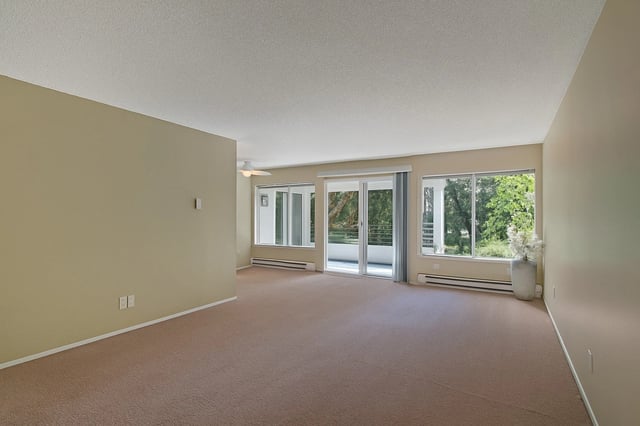 Spacious living room with carpet, large windows, and sliding glass doors leading to a balcony.