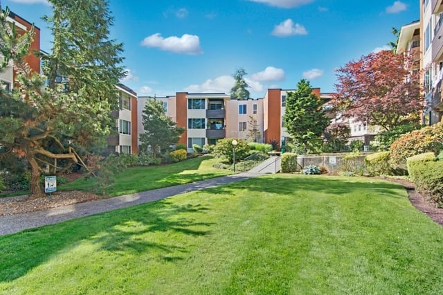 Apartment building exterior with lush green lawns and trees.