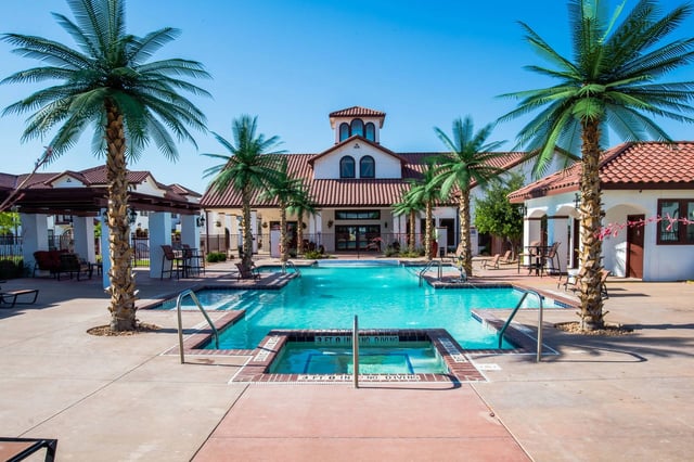 Resort-style swimming pool and hot tub with palm trees and a clubhouse in the background.