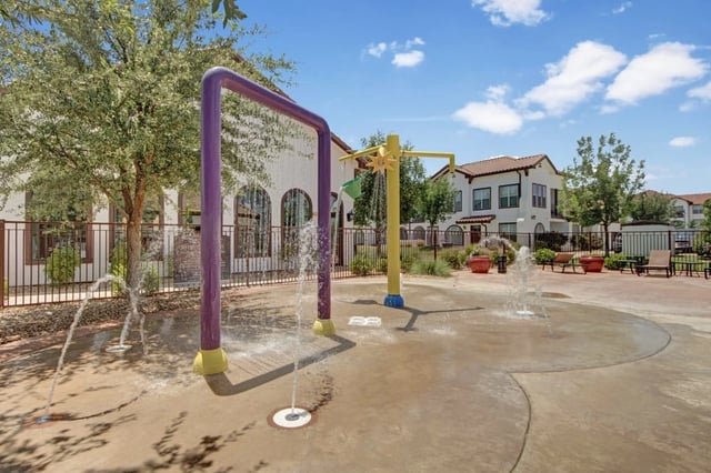 Splash pad with water features and apartment buildings in the background