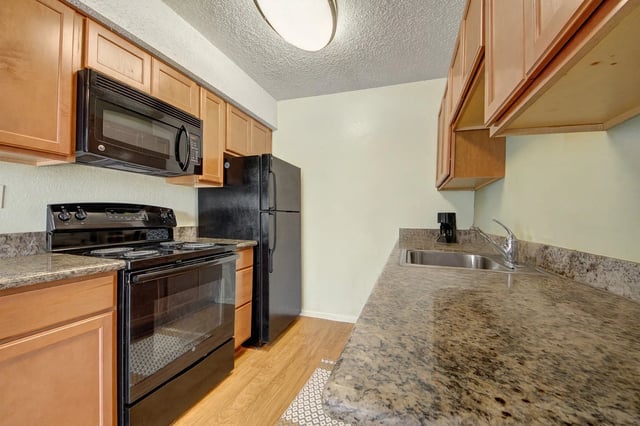 Kitchen with black appliances including a microwave, oven, and refrigerator. Features wood cabinets and granite countertops.