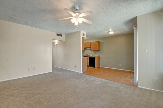 Spacious living area with carpet and a view into the kitchen.