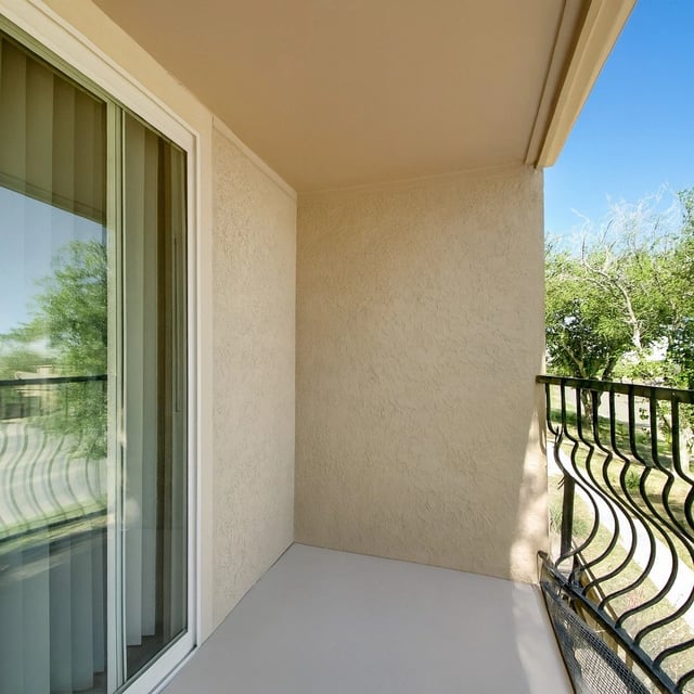 Balcony with sliding glass door and wrought iron railing, overlooking trees.