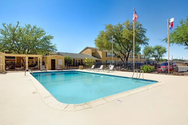 Outdoor swimming pool with lounge chairs and American and Texas flags flying.