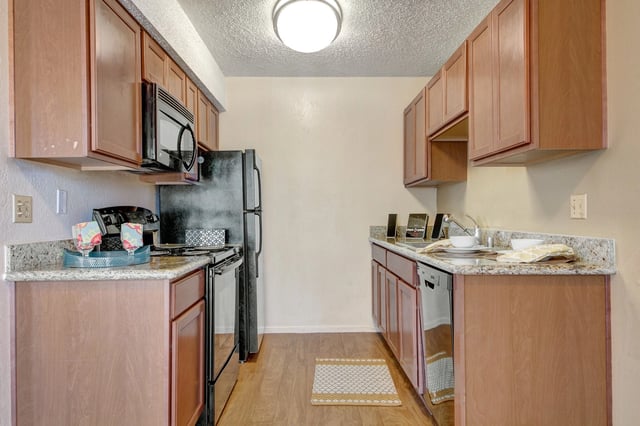 Kitchen with wood cabinets, granite countertops, black appliances, and laminate flooring.