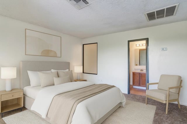 Bedroom with a queen-size bed, nightstand, chair, and view of the bathroom.