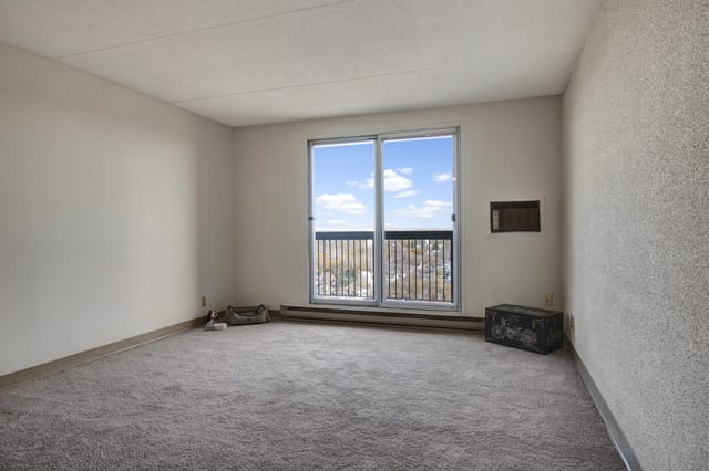 Empty living room with large window overlooking city and balcony.