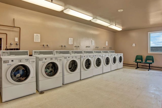 Row of commercial washing machines and dryers in a laundry room.