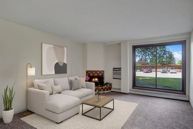 Modern living room with a large sectional sofa, coffee table, fireplace, and a large window overlooking a parking lot.
