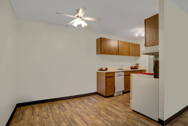 Kitchenette with wood cabinets, white appliances, sink, and wooden flooring.