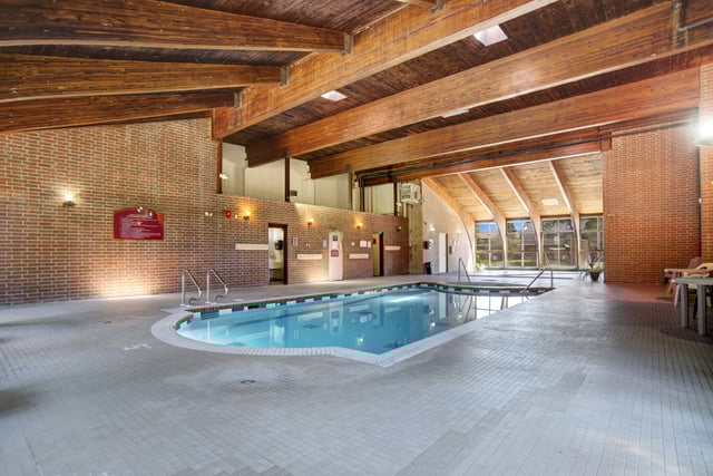 Indoor swimming pool with a vaulted wood-beam ceiling and brick walls.