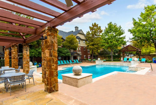 Outdoor community pool with stone pillars, a wooden pergola, and turquoise lounge chairs.