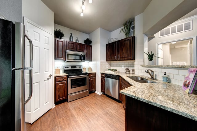 Kitchen in a modern apartment with dark wood cabinets, stainless steel appliances, and granite countertops.