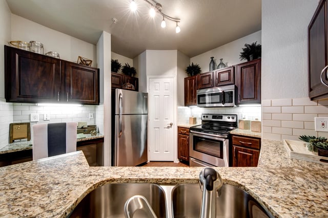 Kitchen in apartment with granite countertops, dark wood cabinets, and stainless steel appliances.