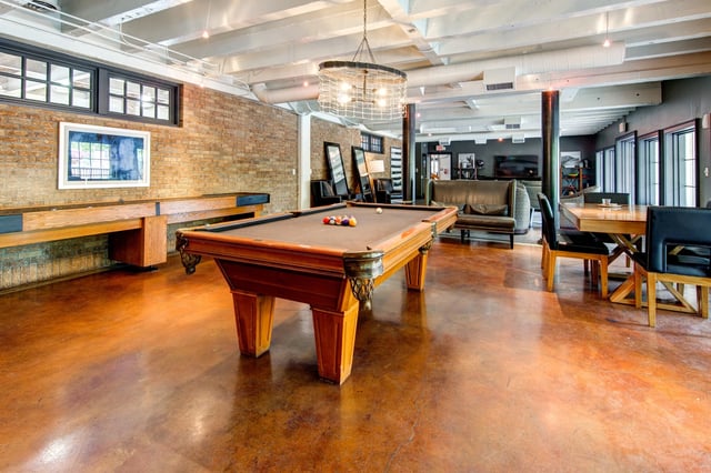 Communal game room with a pool table, lounge seating, and dining area in an industrial-style space.