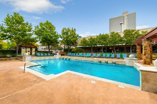 Outdoor pool area at the apartment community with turquoise lounge chairs and trees.