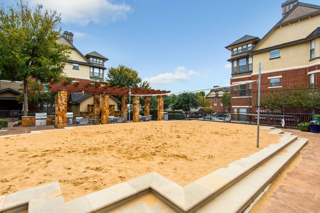 Outdoor communal sand area with a stone pergola, seating, and grills in a residential courtyard.