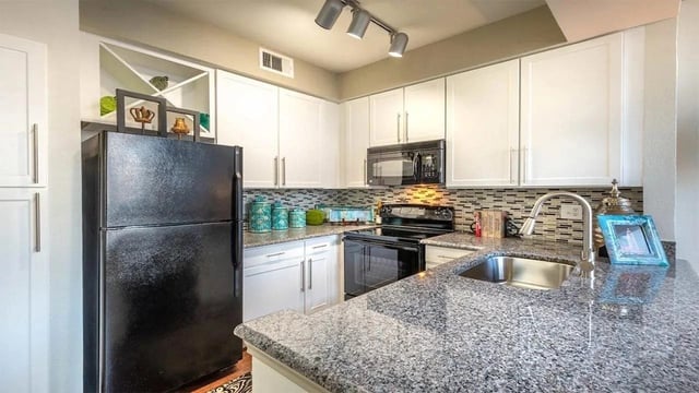 Modern kitchen with white cabinets, granite countertops, black appliances including a refrigerator, oven, and microwave.