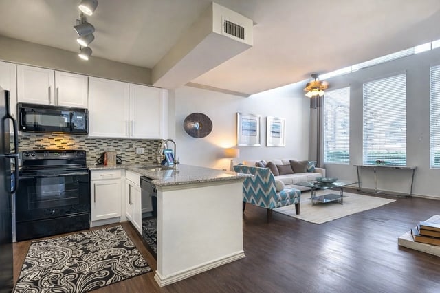 Modern kitchen and living area with sleek white cabinetry, granite countertops, and stylish furnishings.