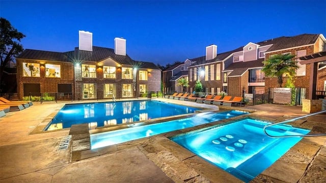 Luxury apartment complex with a bright blue swimming pool and hot tub at dusk.