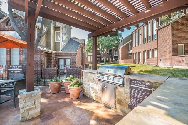 Outdoor grilling area with built-in stainless steel grill, stone counter, and seating area under a pergola.