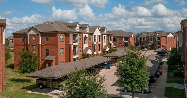 Apartment building exterior with covered parking and trees.
