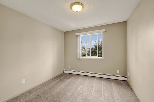 Empty bedroom with neutral carpet and beige walls, a large window with white blinds overlooks trees.