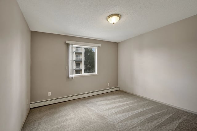 Empty bedroom with neutral carpet and beige walls, window overlooking building exterior.