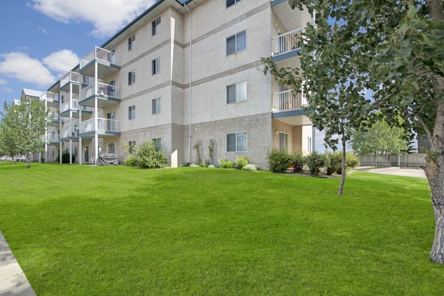 Exterior view of a multifamily building with balconies and a large green lawn.