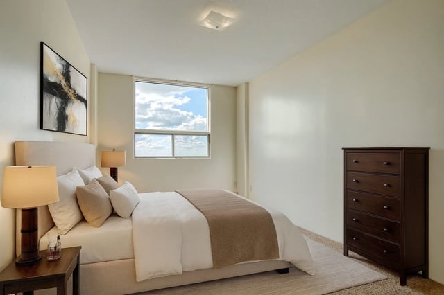 Cozy bedroom with a queen-size bed, nightstand with lamp, and dresser.