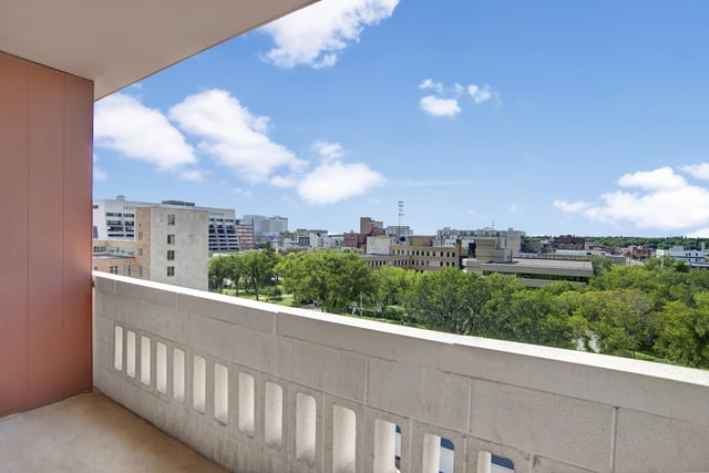 Balcony view of city skyline with green trees and blue sky with clouds.