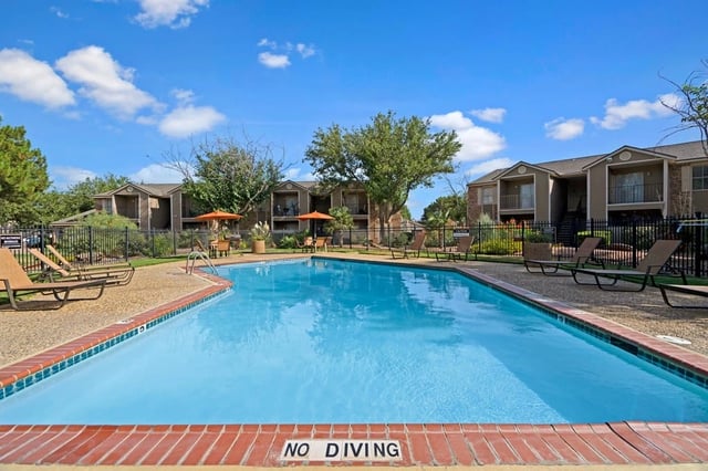 Swimming pool and lounge chairs at apartment complex on a sunny day.