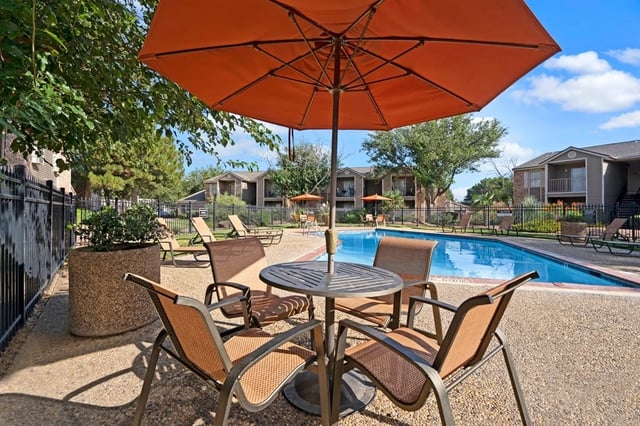 Outdoor swimming pool with lounge chairs and a table with an umbrella.