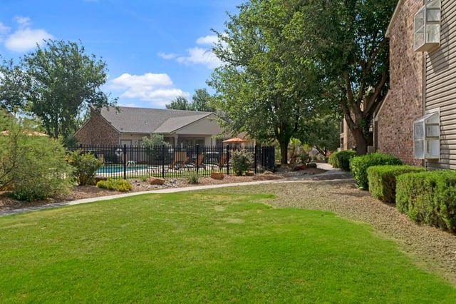Outdoor swimming pool area with lounge chairs and umbrellas, surrounded by a black fence and lush greenery.