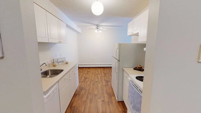 Kitchen with white cabinets, sink, dishwasher, and refrigerator, opening to a living area.