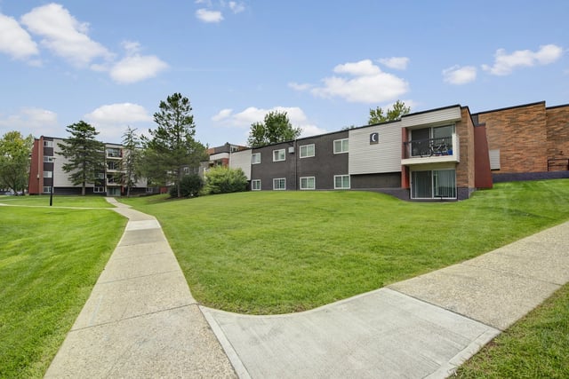 Exterior view of apartment buildings with a paved walkway through a grassy area.