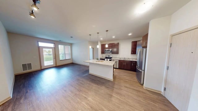 Modern kitchen with island and stainless steel appliances, open to living area.