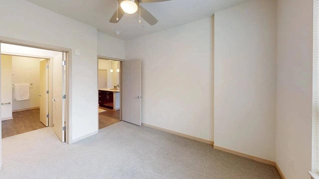 Bedroom with a ceiling fan and views into a bathroom and kitchen area.