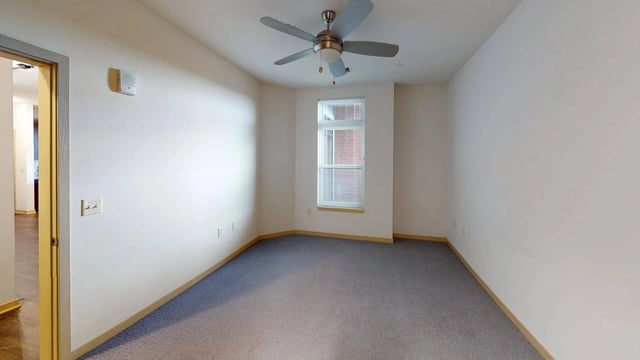 Interior view of an empty apartment bedroom with a ceiling fan and a window.