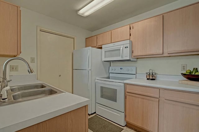 Kitchen with light wood cabinets, white countertops, double sink, and white appliances.