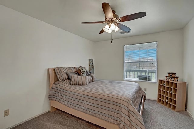 Bed with striped comforter and pillows in a bedroom with a ceiling fan and a window.