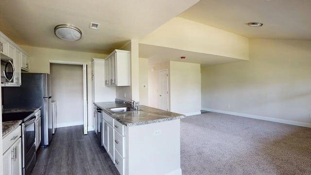 Modern kitchen with stainless steel appliances and granite countertops, open to a spacious living area.